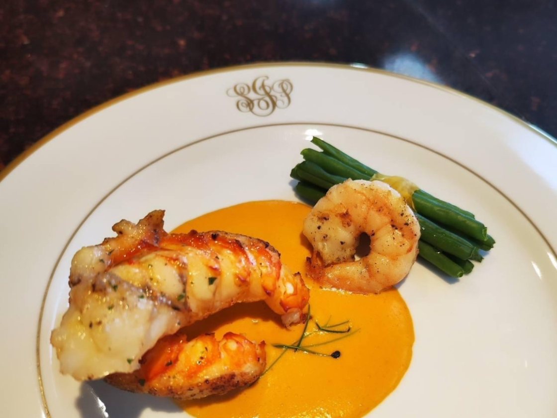 A butter-poached lobster tail with prawns and green beans in bisque