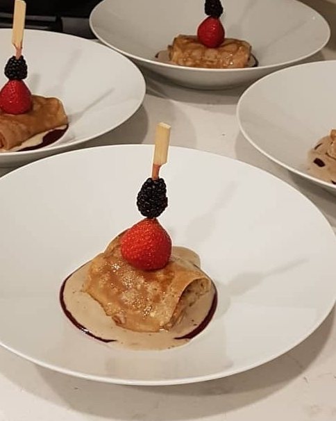 Crêpes rolled and topped with berries, plated one to a guest